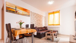 A modern living room with a dining area, featuring a fireplace, a stone accent wall, and a large window with curtains. - Apartments Jasmina (Rovinj)