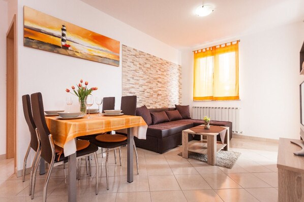 A modern living room with a dining area, featuring a fireplace, a stone accent wall, and a large window with curtains.