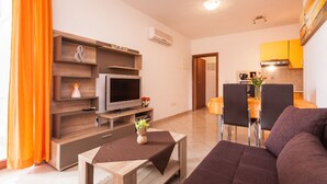 A modern living room with a flat-screen TV, wooden shelving, a sofa, and a dining area with chairs and a table. - Apartments Jasmina (Rovinj)