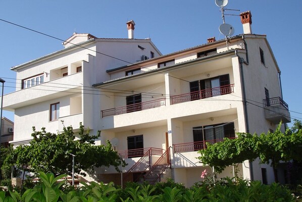 A multi-story residential building with balconies, satellite dishes, and a garden area in the foreground. - Apartments Jasmina (Rovinj)