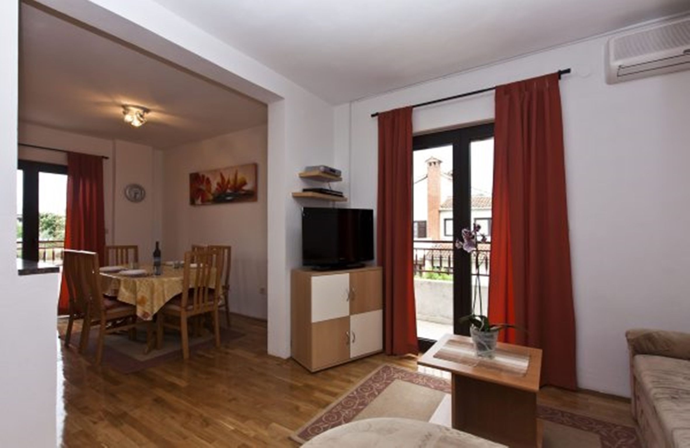 Ein Wohnzimmer mit einem Holzesstisch, Stühlen, einem Fernseher auf einem Schrank und einem Sofa.