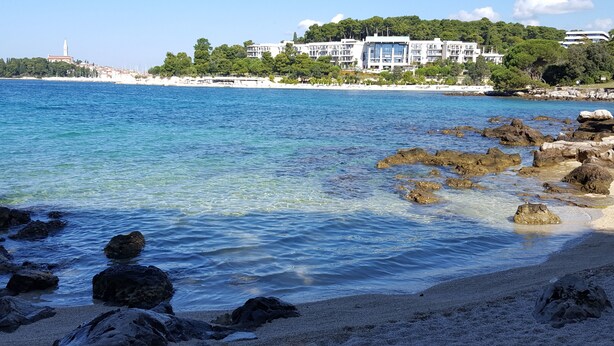 A coastal view with clear blue waters, rocky shoreline, and a building with multiple balconies overlooking the sea. - Apartments Jasmina (Rovinj)