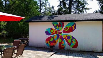 A wooden deck with a colorful flower mural on a building wall, outdoor seating, and a red umbrella.