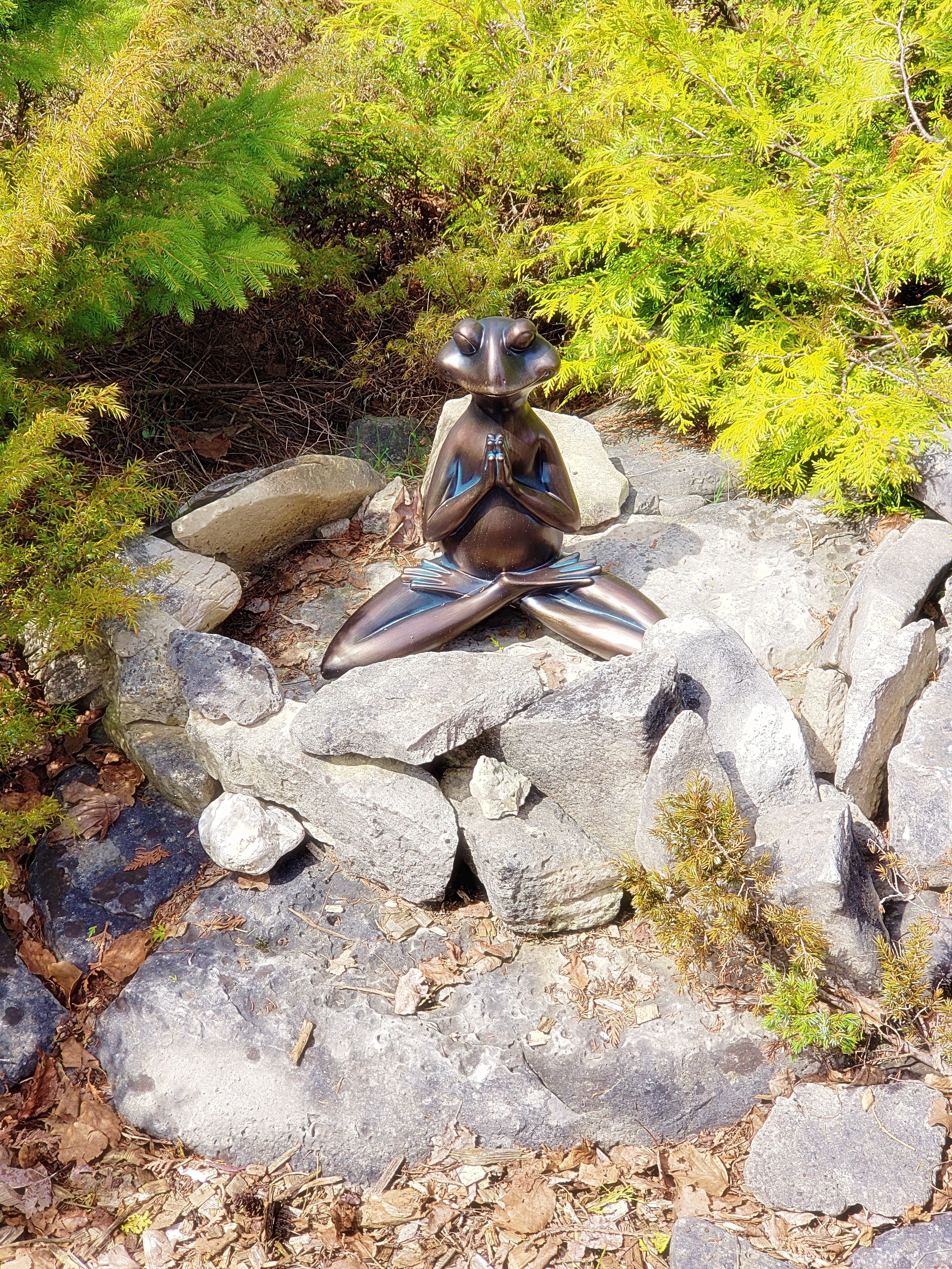 A sculpture of a seated figure in a meditative pose on rocks surrounded by greenery.