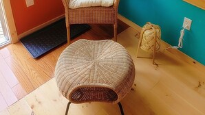 A room with a wicker chair and ottoman, a teal accent wall, a hanging macrame plant, and a window with a view of an outdoor area. - Buddha Bing Cottage and Cabins (Northern Bruce Peninsula)