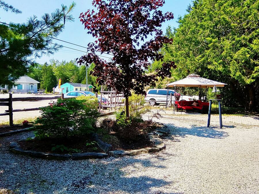 A gravel parking area with a gazebo, a red car, and a white van.
