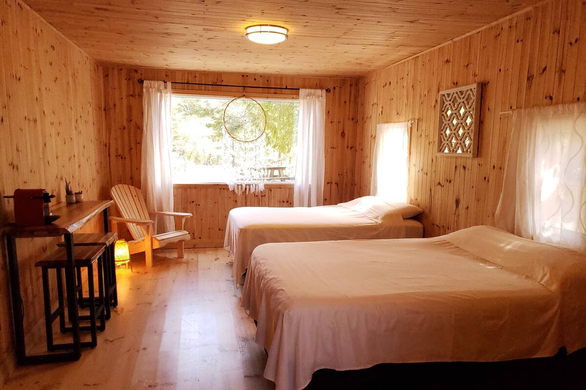 A wooden cabin room with two beds, a desk, and a chair.