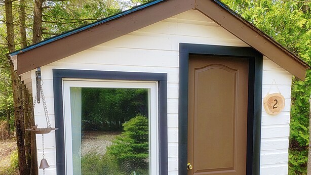 A small, single-story cabin with a large window, a door, and a number '2' sign. - Buddha Bing Cottage and Cabins (Northern Bruce Peninsula)