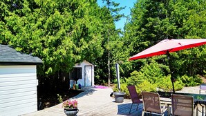 A wooden deck with outdoor furniture, a red umbrella, and a small shed. - Buddha Bing Cottage and Cabins (Northern Bruce Peninsula)