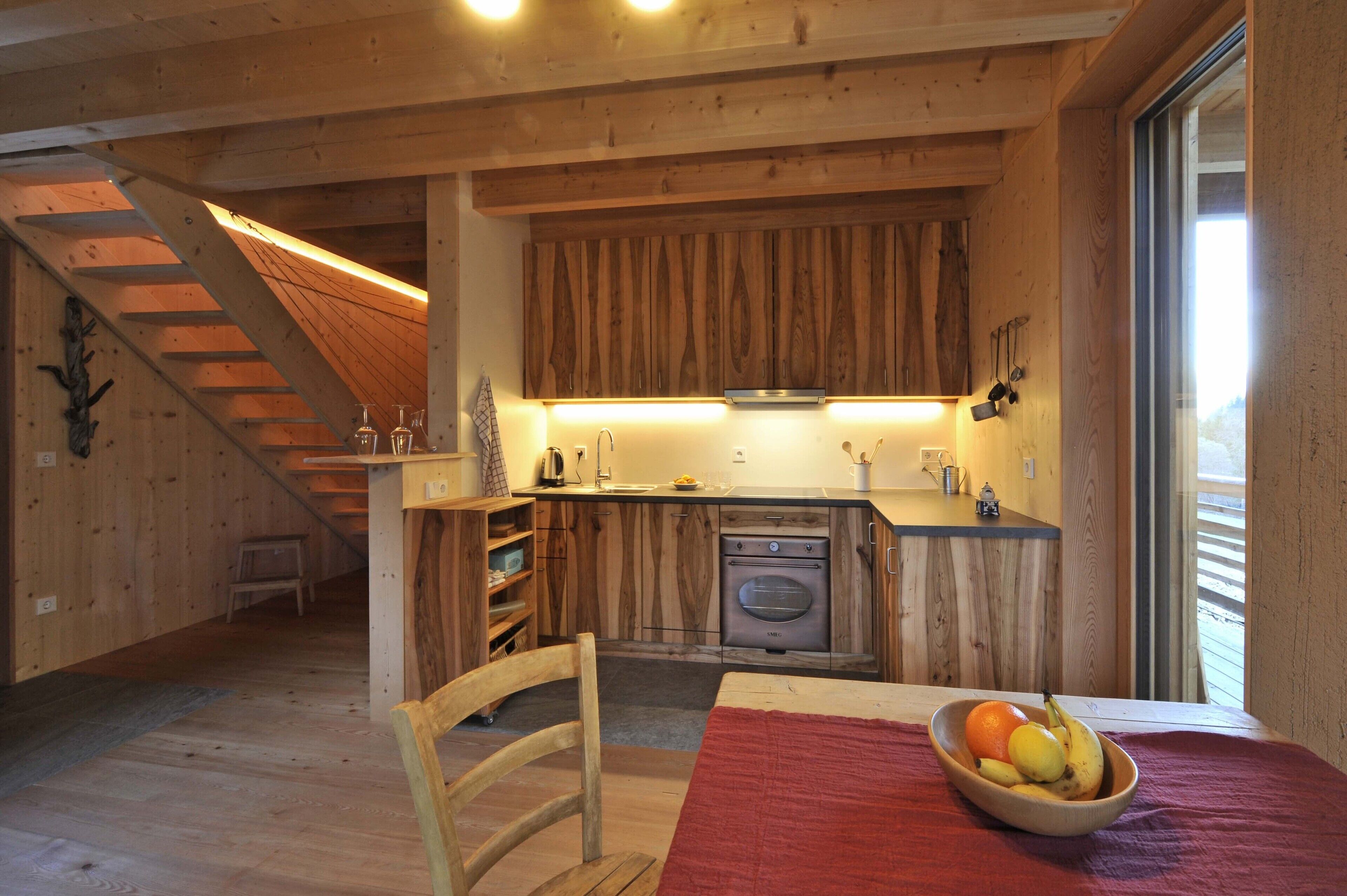 Un intérieur en bois comprenant un coin cuisine, une table à manger avec un saladier de fruits et un escalier.