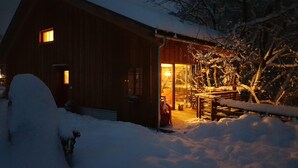 Eine Holzhütte mit verschneitem Dach und beleuchtetem Innenraum.