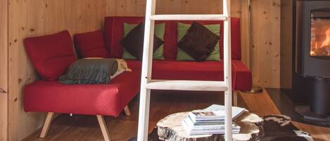 A wooden cabin interior with a wooden ladder, red sofa, and a fireplace.