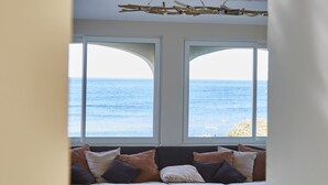 Een moderne woonkamer met een groot raam met uitzicht op zee, een bijzondere plafondlamp en een gezellig zithoekje.