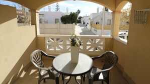 Een balkon met een ronde tafel en twee stoelen, een witte balustrade en uitzicht op een woonstraat.