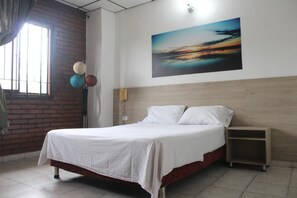 Una habitación de hotel con cama, mesita de noche, un cuadro en la pared y ventana con vistas.
