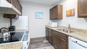 Une cuisine moderne dotée de plans de travail en granit, d’armoires en bois, d’un four à micro-ondes encastré, d’une plaque de cuisson et d’un lave-vaisselle.