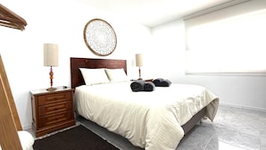 Ein Hotelzimmer mit Bett, Nachttisch aus Holz, zwei Nachttischlampen, einer Wanddekoration und einem Fenster.