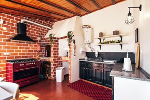 A kitchen with a brick wall, a gas stove, black cabinets, and a wooden ceiling.