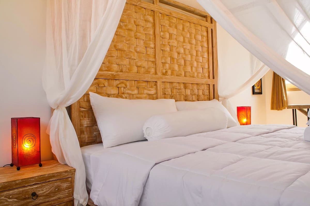 A neatly made bed with white linens, a wooden headboard with a woven pattern, and two bedside lamps.