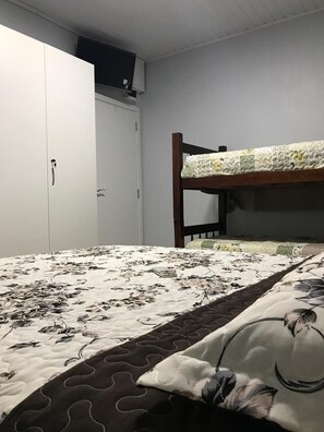 Uma cama de solteiro com edredom estampado de flores, um guarda-roupa branco e uma pequena prateleira sobre a cama.