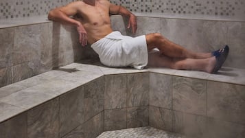 A person sitting in a steam room with tiled walls and a tiled floor.