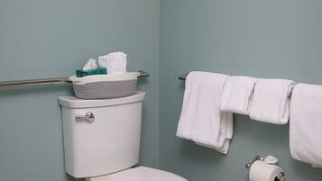 A bathroom with a toilet, a towel rack with towels, a toilet paper holder, and a wall-mounted light fixture.