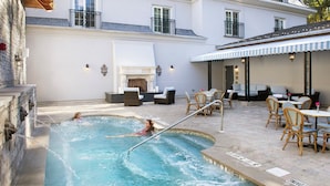 A swimming pool with a person in the water, surrounded by outdoor furniture and a building with a balcony.