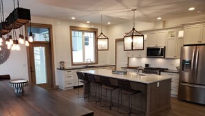 Een moderne keuken met een centraal eiland, barkrukken, roestvrijstalen apparatuur en hanglampen.