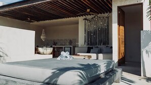 A modern outdoor bedroom with a concrete bed, a wooden ceiling, and a view of a kitchen and dining area. - Gated Jungle Lounge • Wabi Sabi Chic Two -Level Penthouse + Private Plunge Pool  (Tulum)