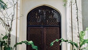 A large, ornate wooden door with intricate lattice patterns, flanked by lush green plants and a concrete staircase leading up to it. - Gated Jungle Lounge • Wabi Sabi Chic Two -Level Penthouse + Private Plunge Pool  (Tulum)
