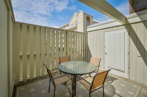 Eine Terrasse mit einem runden Glastisch und vier Stühlen, einer weißen Tür und einem weißen Zaun.