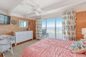 Ein Schlafzimmer mit Bett, Kommode, Stuhl und einem großen Fenster mit Vorhängen.