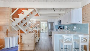 Una cocina moderna con armarios blancos, un refrigerador de acero inoxidable y una escalera de madera.