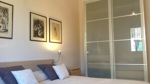 Ein Schlafzimmer mit einem Bett, Kissen, einem Nachttisch, einer Lampe und gerahmten Kunstwerken an der Wand.