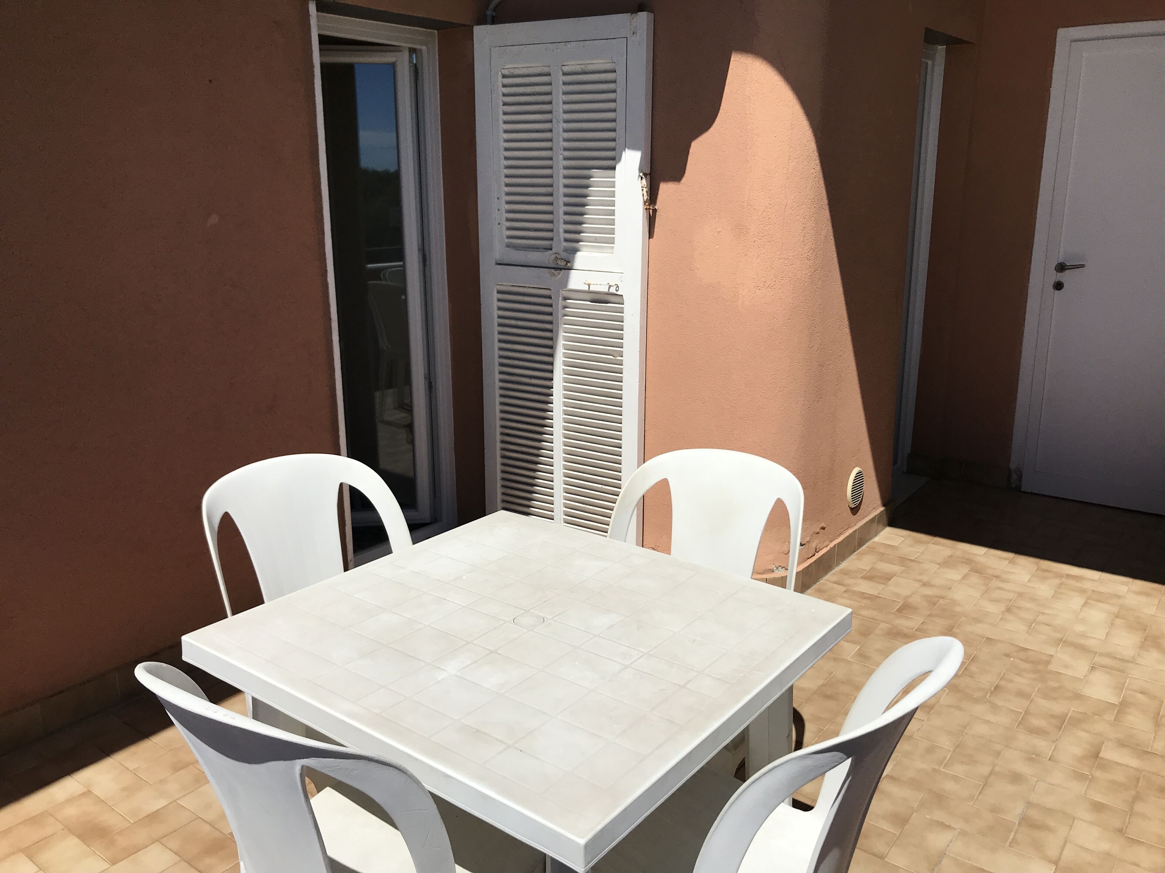 En terrasse med et hvidt bord og stole, en skydedør samt en lukket dør.