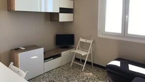 Ein gemütlicher Wohnbereich mit Küchenzeile, einem Fernseher, einem weißen Stuhl und einem Fenster.