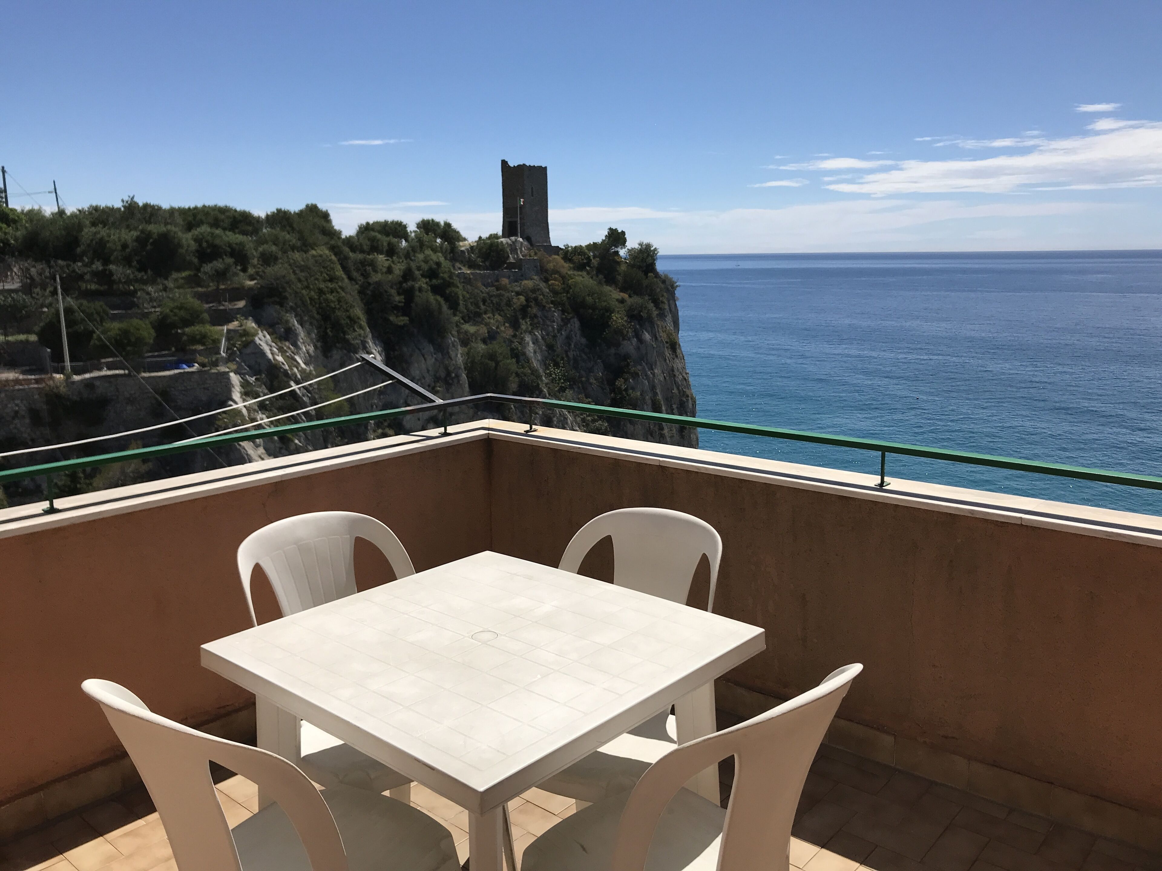 Een balkon met tafel en stoelen, met uitzicht op de kust en een toren.