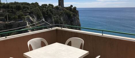 A balcony with a table and chairs overlooking a coastal view with a tower.