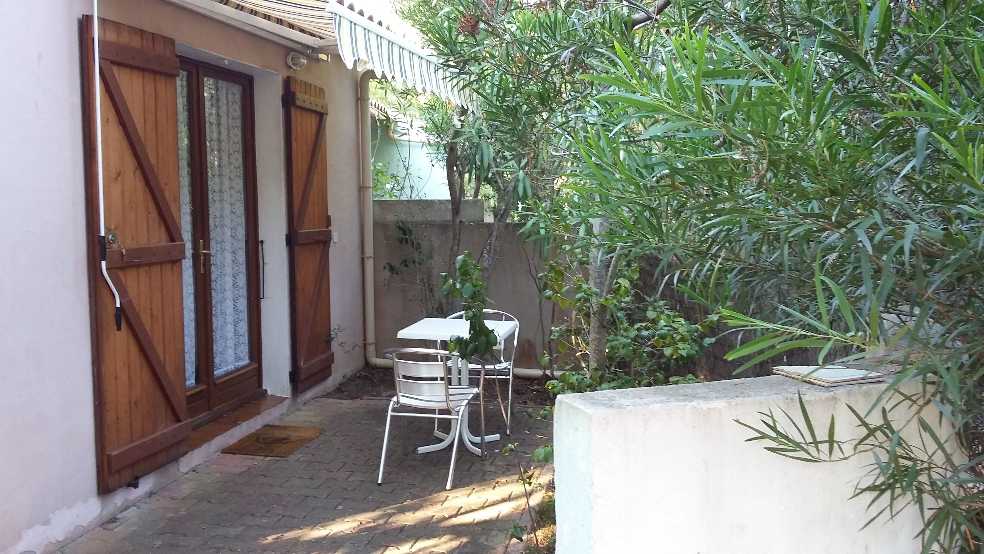 Une petite terrasse avec une table et des chaises, une porte en bois et un mur en béton.