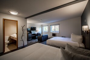 A hotel room with two beds, a desk, a chair, a TV, and a bathroom.
