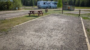 Ein Campingplatz mit Picknicktischen, einem Kiesparkplatz und einem Wohnmobil im Hintergrund.