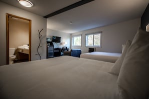 A hotel room with two beds, a desk with a chair, a television, and a window.