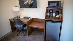 Ein Hotelzimmer mit Schreibtisch, Stuhl, Flachbildfernseher, Mikrowelle, Kaffeemaschine und Minikühlschrank.