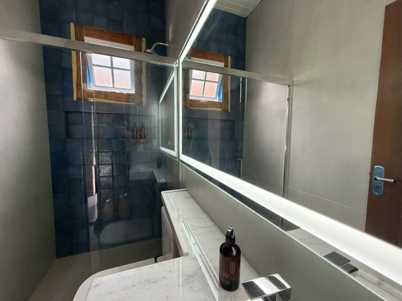 Een moderne badkamer met een douchecabine van glas, een wit aanrechtblad en een fles shampoo.
