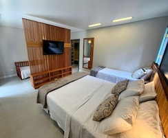 Quarto moderno com uma cama grande, TV presa a um painel de madeira, guarda-roupa e espelho.