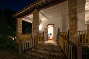 Um edifício de pedra com varanda coberta e escadaria que leva à entrada.