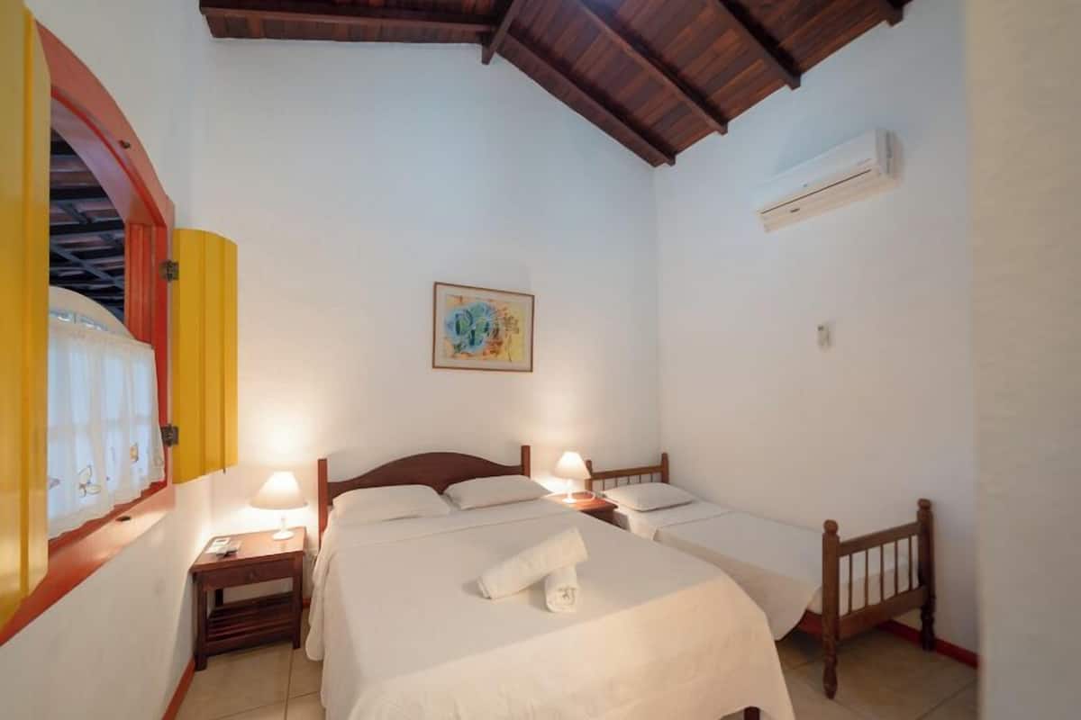 A hotel room with two beds, a wooden ceiling, an air conditioning unit, and a painting on the wall.