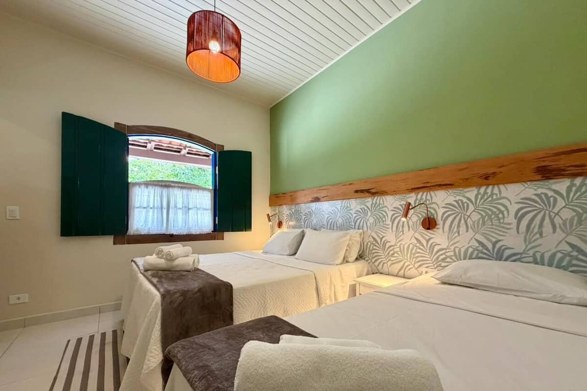 A hotel room with two beds, a window with green shutters, a wooden headboard, and a striped rug.