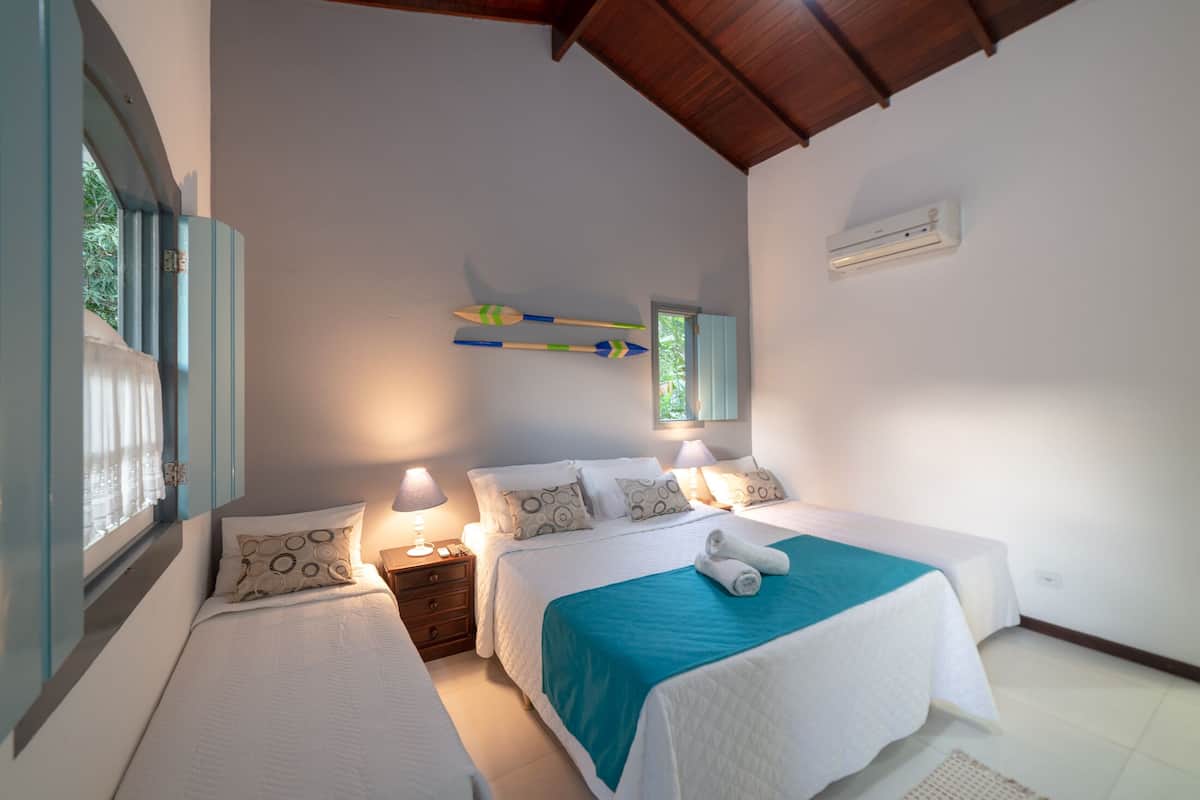 A bedroom with two beds, a window with curtains, an air conditioning unit, and a wall-mounted decoration.