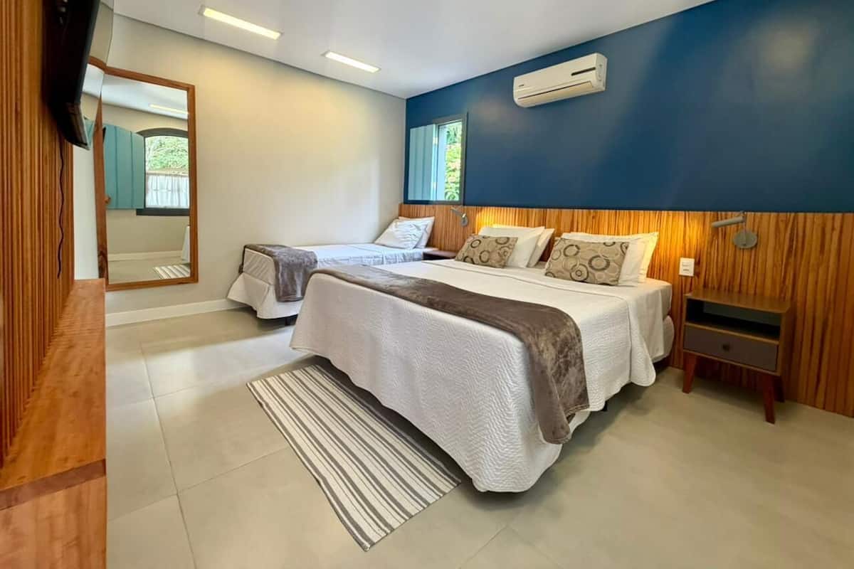 A modern bedroom with two beds, a TV, an air conditioner, and a wooden accent wall.